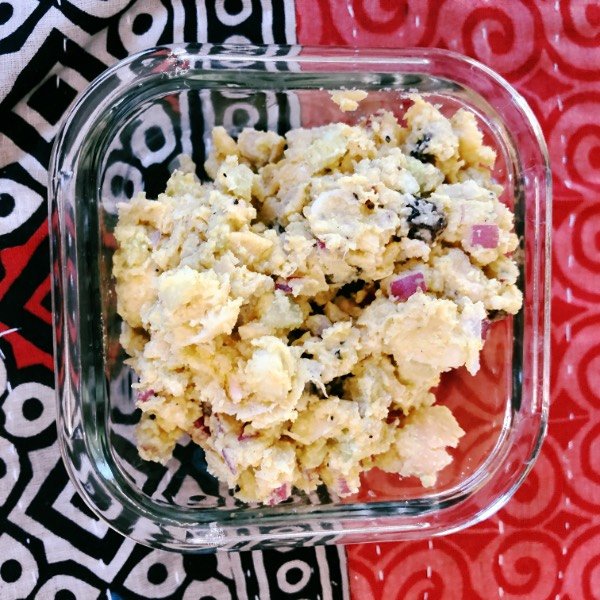curried chickpea salad in a square glass container on a colorful background.