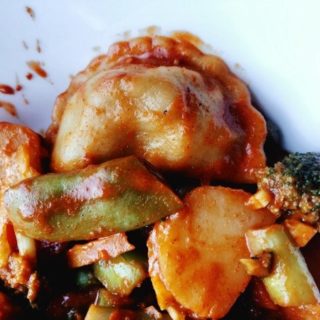 close up of korean dumpling stir-fry in a white bowl with a clearly visible dumpling.