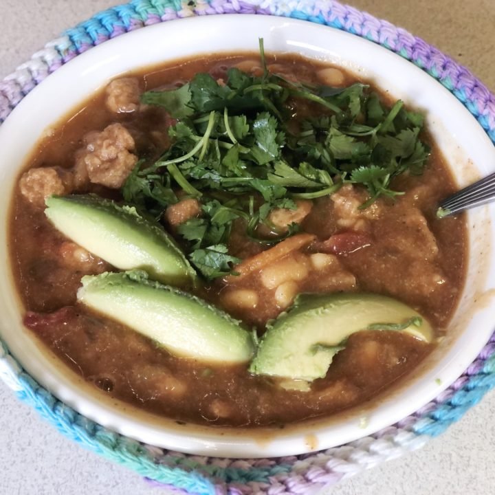 vegan chicken chili in a white bowl topped with cilantro and avocado slices.