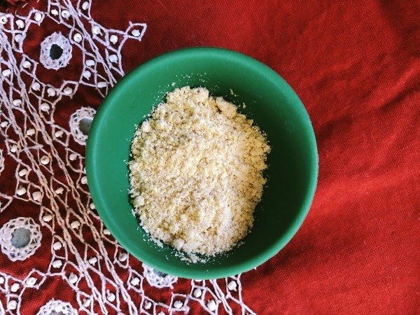 a green bowl full of vegan parmesan on a red placemat.