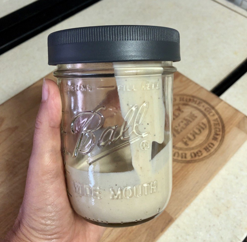 oil free tahini dressing in a glass mason jar with a grey plastic lid.