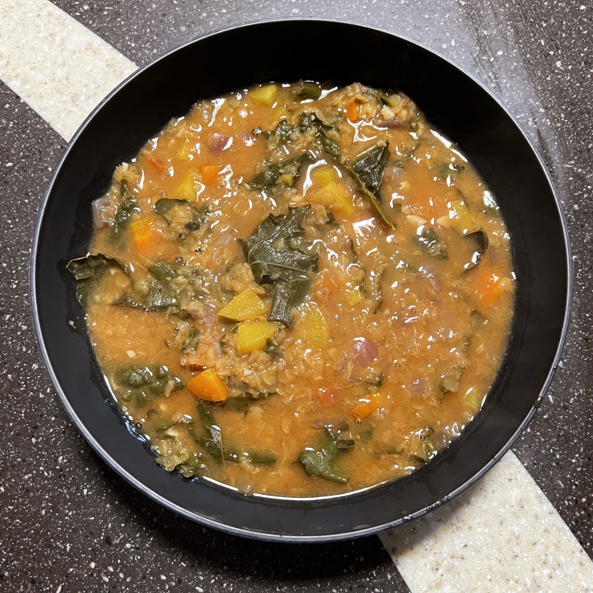 a black bowl containing red lentil soup with kale.