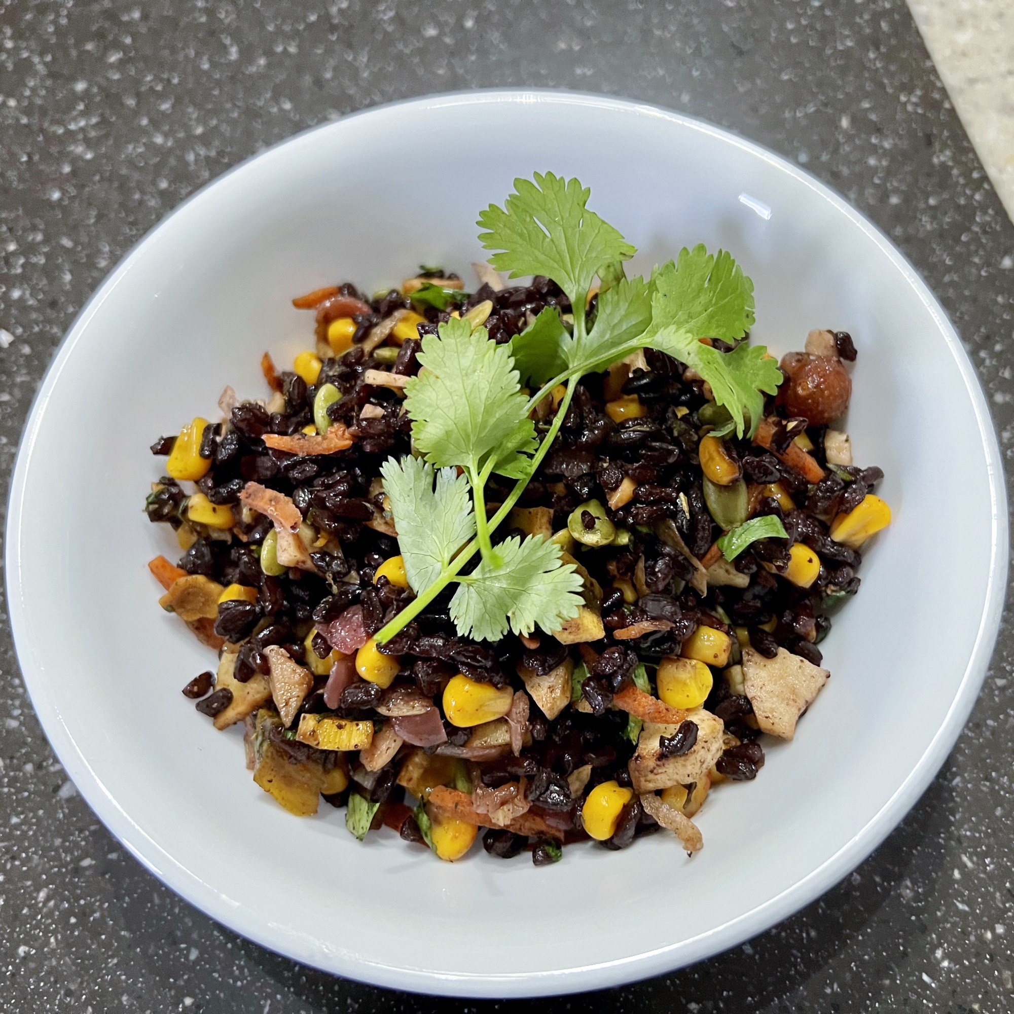 autumn black rice salad in a white bowl garnished with a cilantro sprig.
