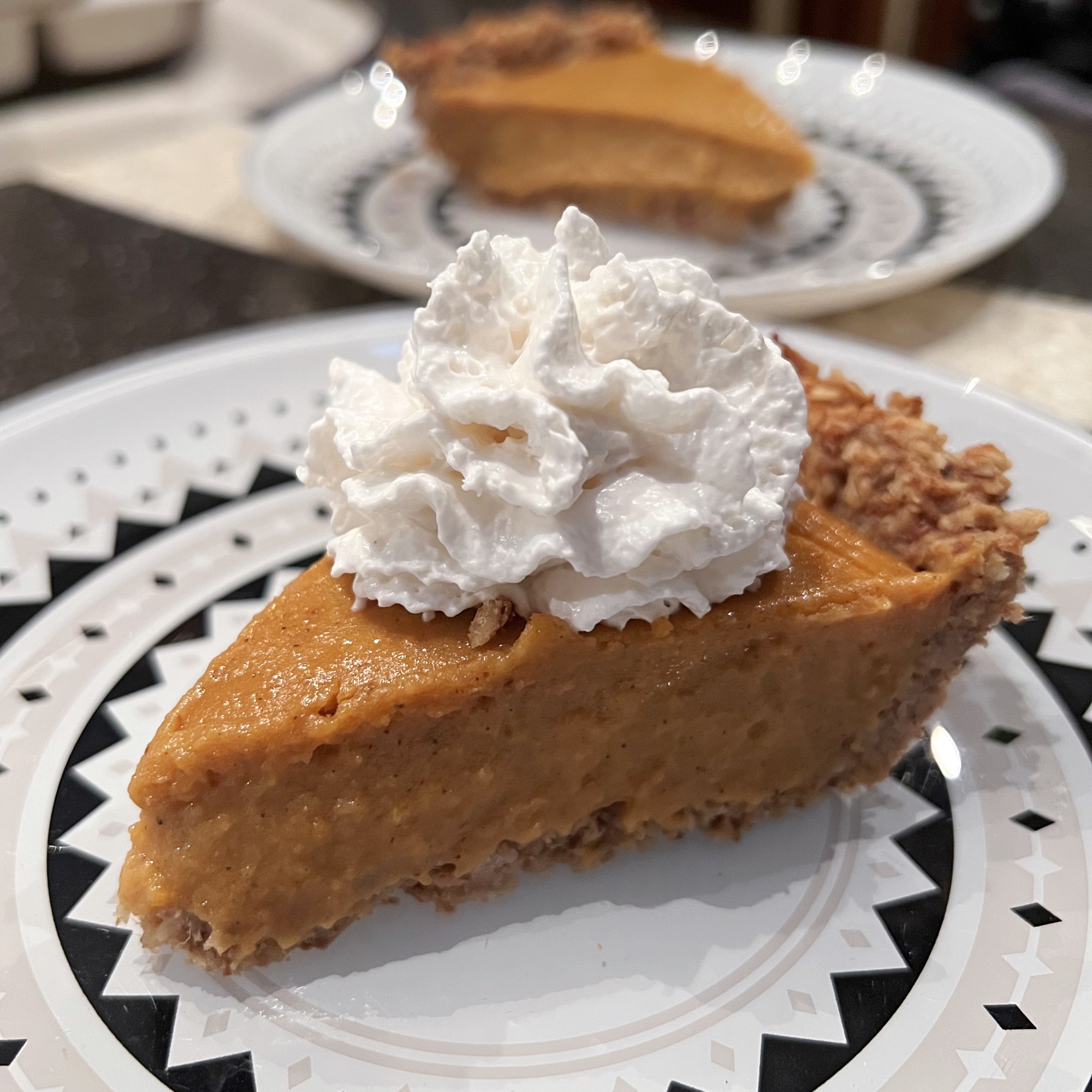 a slice of vegan and gluten free sweet potato pie on a black and white plate with vegan whipped cream on top.