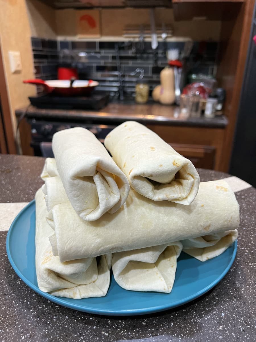 8 freshly rolled burritos stacked on a blue plate.