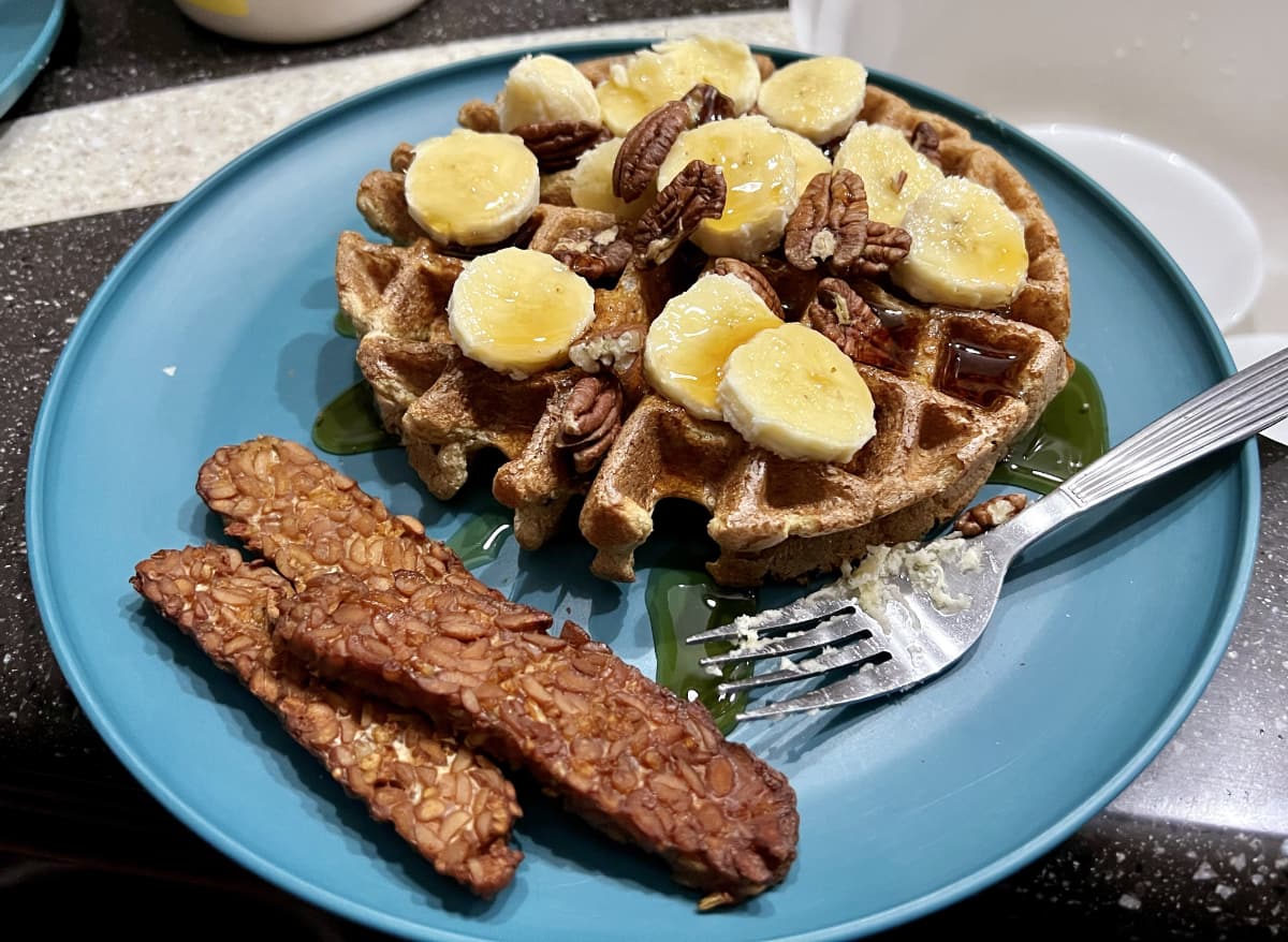vegan belgian waffle topped with bananas with tempeh bacon.